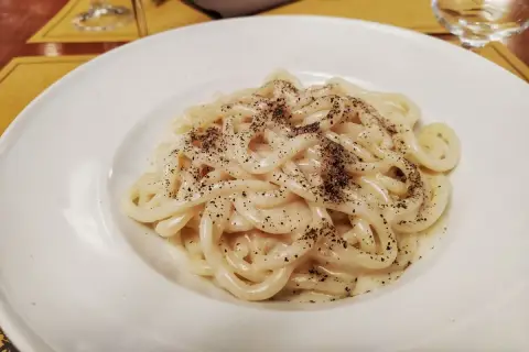 Pici cacio e pepe, un classico piatto romano, servito in un piatto bianco.
