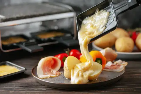 Formaggio fuso in padella, filante e dorato, viene versato su patate e salumi. Un piatto invitante e gustoso.