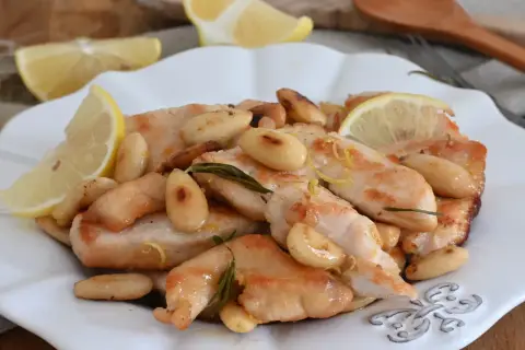 Succulento pollo al limone con mandorle tostate e rosmarino, guarnito con spicchi di limone fresco.