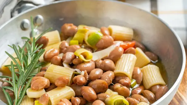 Minestra di fagioli con pasta rigata, cipollotto e rosmarino in una padella.