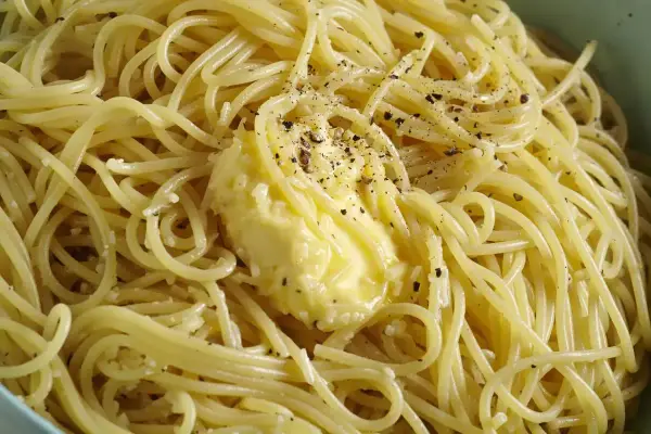 Spaghetti fumanti con burro fuso e pepe nero macinato, pronti per la cacio e pepe ricetta originale romana.