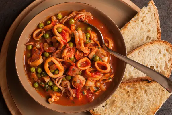 Calamari al sugo con piselli, un piatto saporito servito in una ciotola con pane tostato.